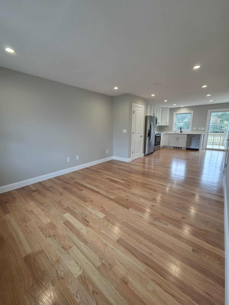 Empty modern kitchen and living area with hardwood floors and recessed lighting.
