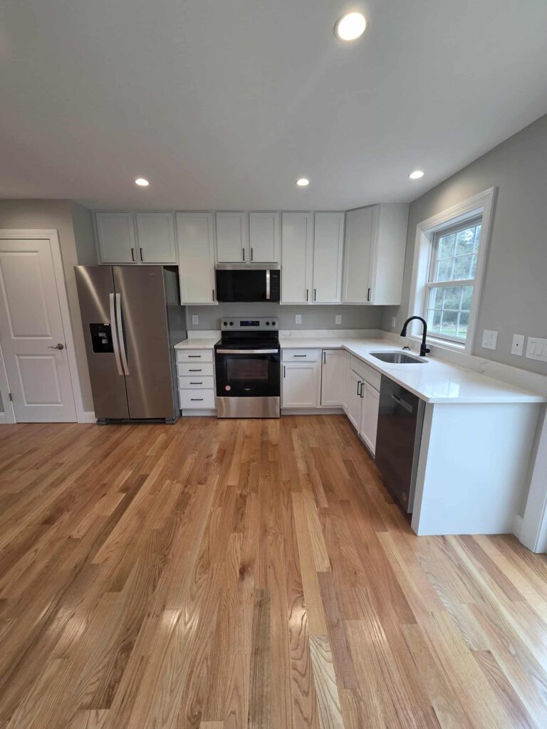 Modern kitchen with white cabinets, stainless steel appliances, and hardwood floors.