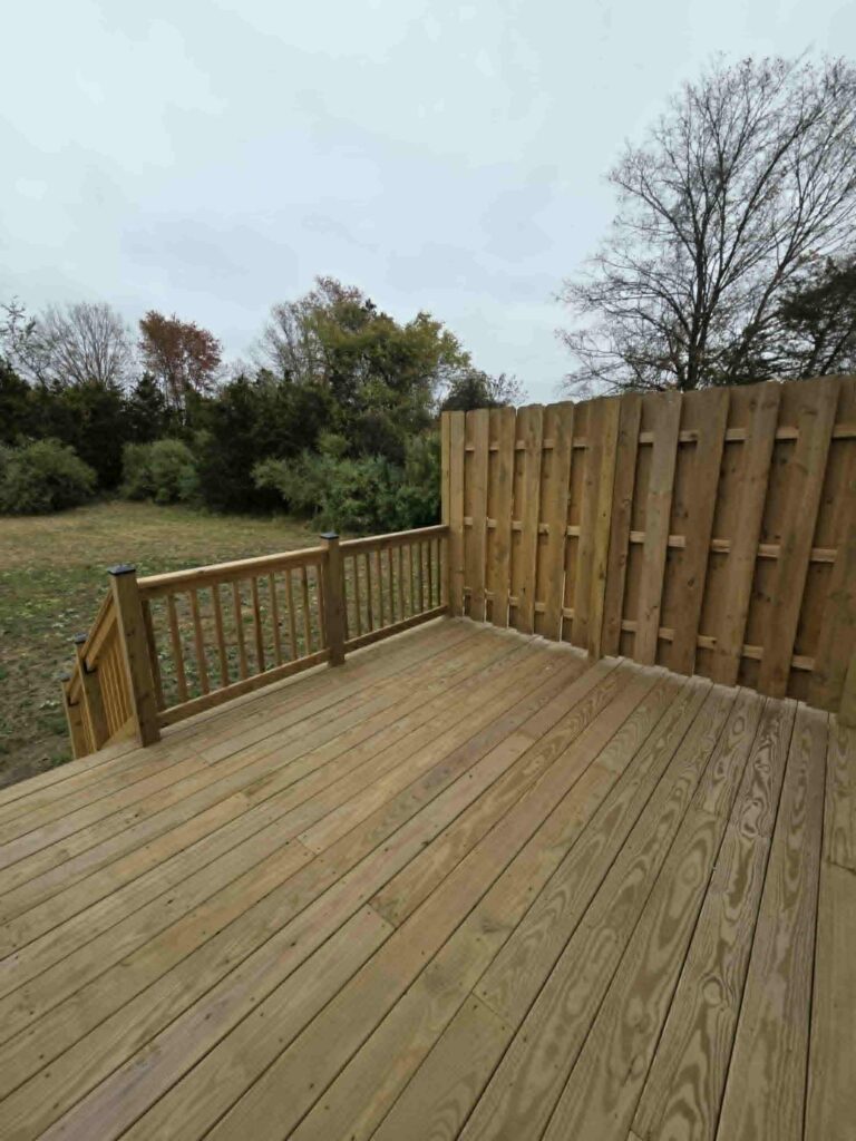 Wooden deck with railing overlooking a grassy backyard and trees.