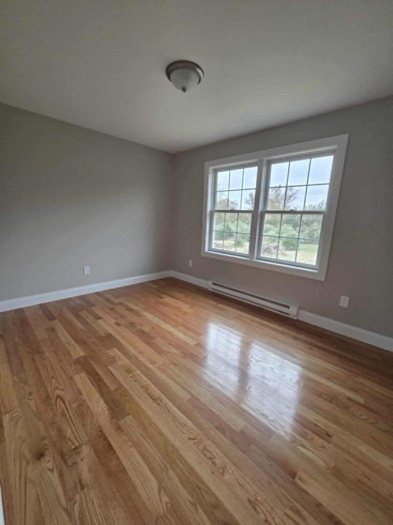 Empty room with hardwood floors and large window letting in natural light.