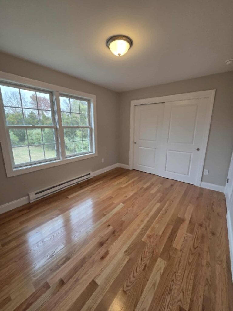 Empty room with polished hardwood floors and large windows.