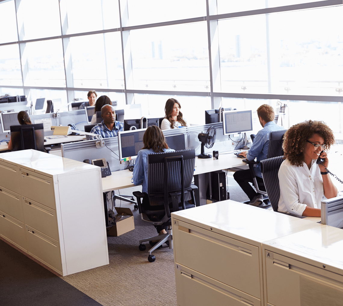 Busy modern office with employees working at desks near large windows.
